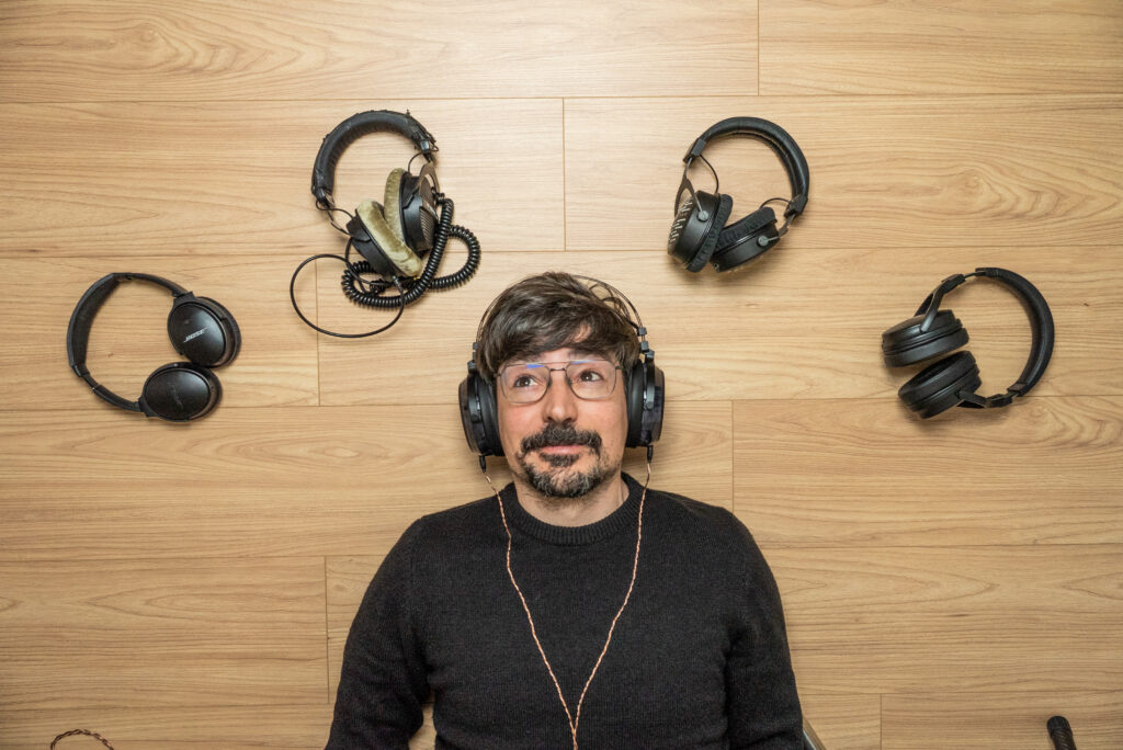 WasabiNoise listening music on headphones with multiple headphones around him